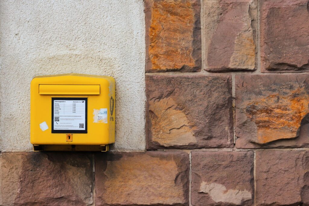 a yellow mailbox mounted on a rustic stone wall, displaying postal information.