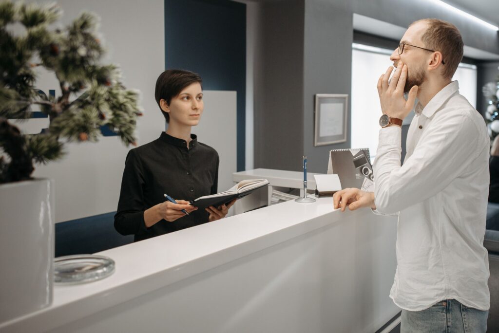a receptionist assists a patient with a toothache at a dental clinic's front desk.