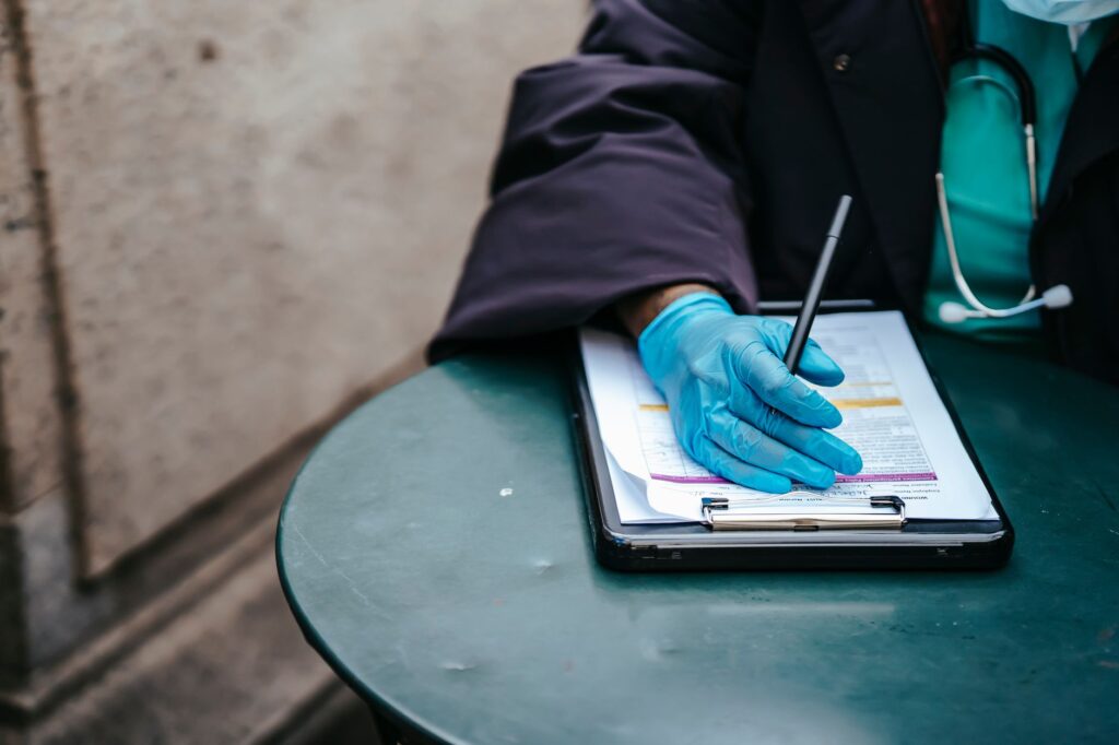 crop anonymous ethnic female physician in disposable glove with paper on clipboard working at table in daylight