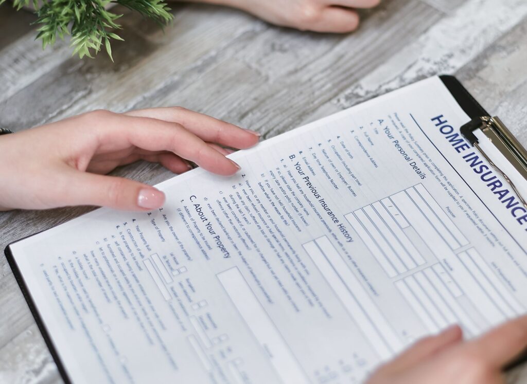close-up of hands holding a home insurance document indoors, showing personal details section.