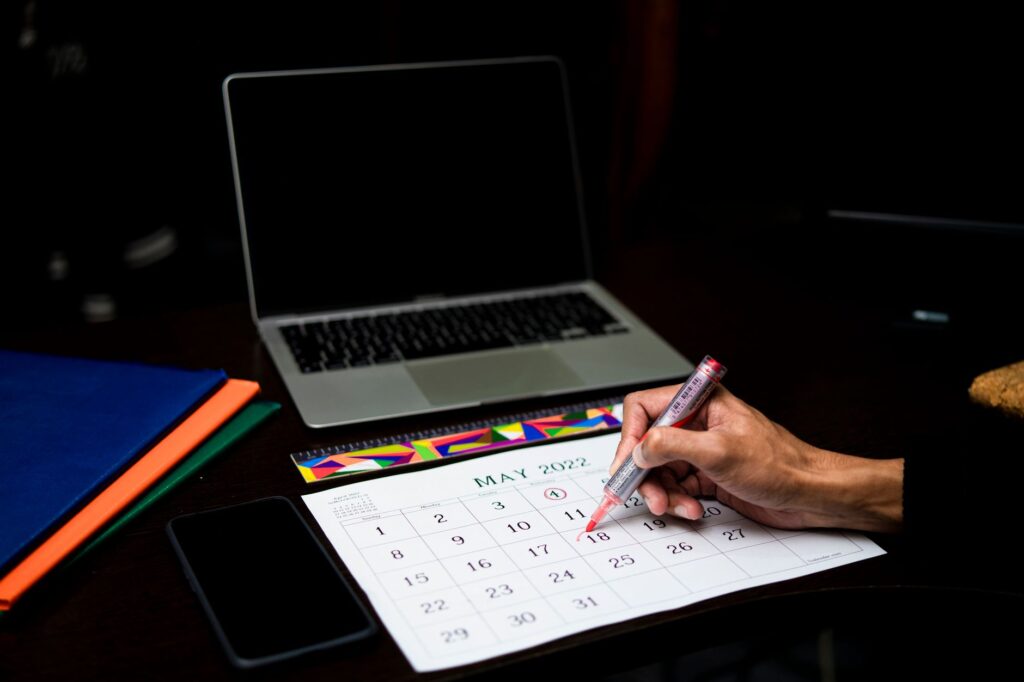a person plans on a calendar at a desk with a laptop and phone, may 2022.