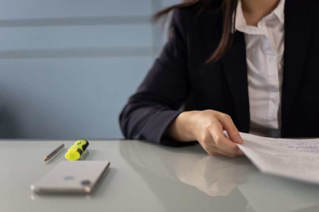 business professional reviewing documents with highlighter and phone on glass desk, ideal for office scenes.