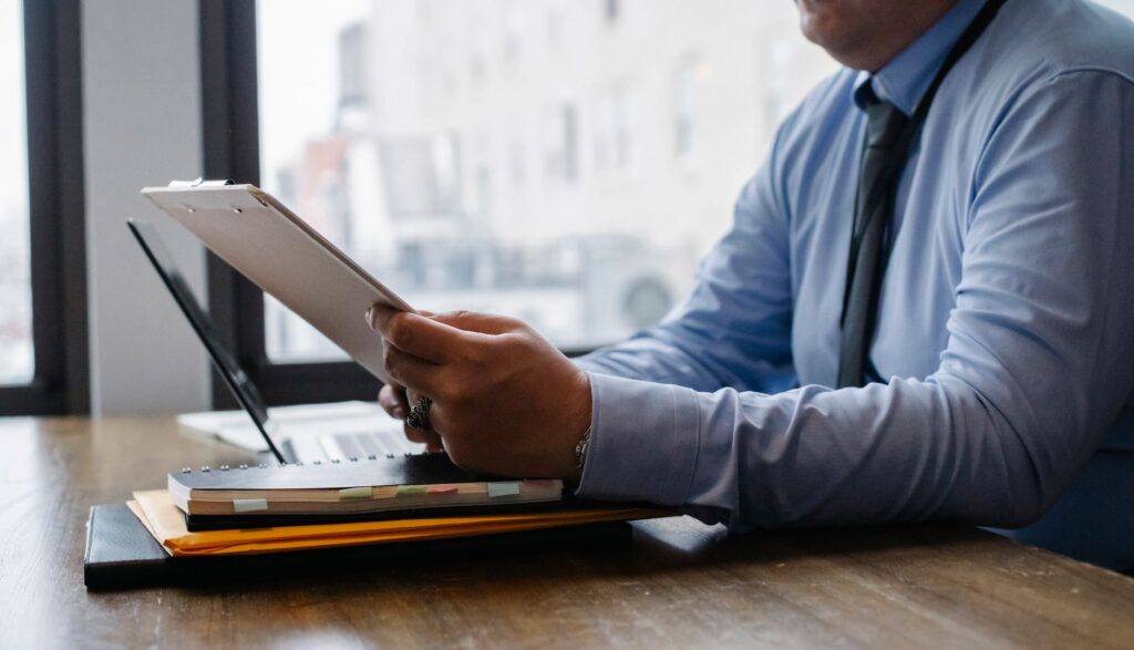 crop unrecognizable male manager wearing blue shirt and black tie sitting at wooden desk and reading financial informati