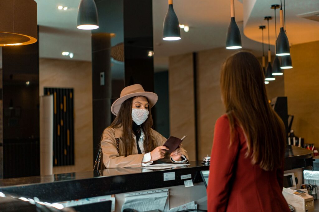 a woman wearing a mask checks in at a hotel reception desk.