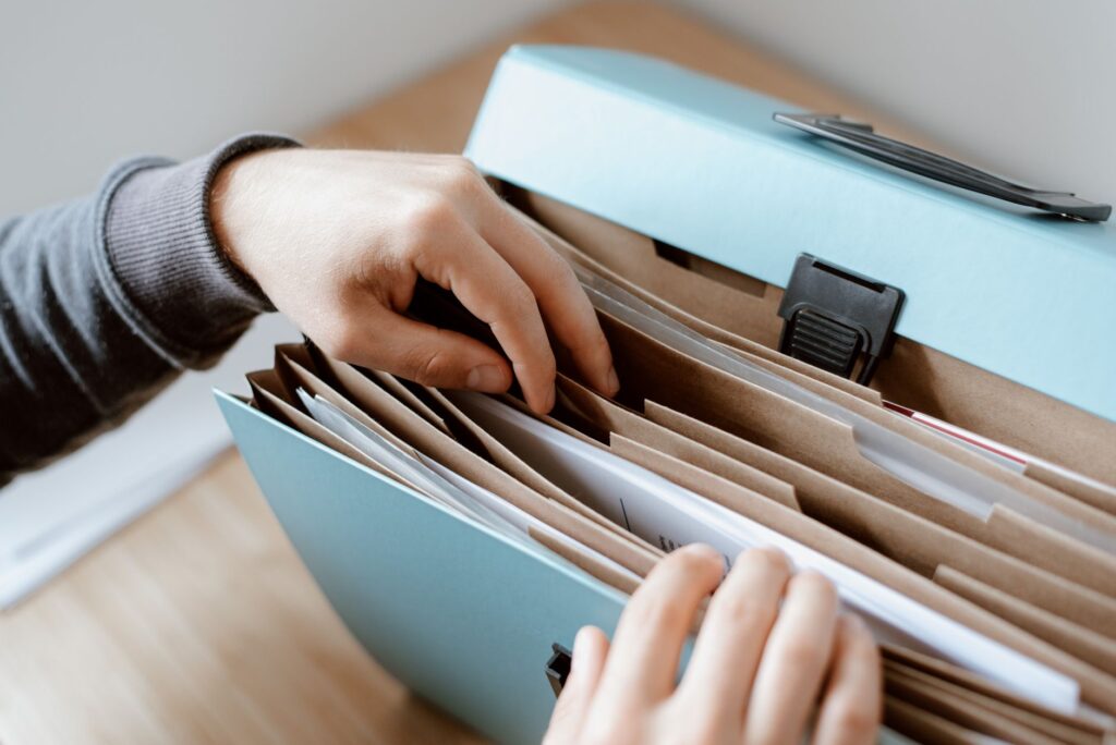 crop unrecognizable person selecting document in opened briefcase for documents placed on wooden table