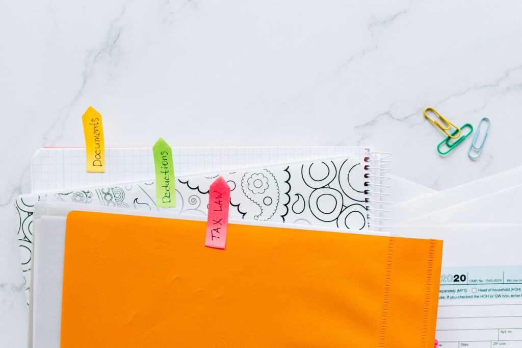 top view of tax documents organized with colorful sticky notes on a marble desk.