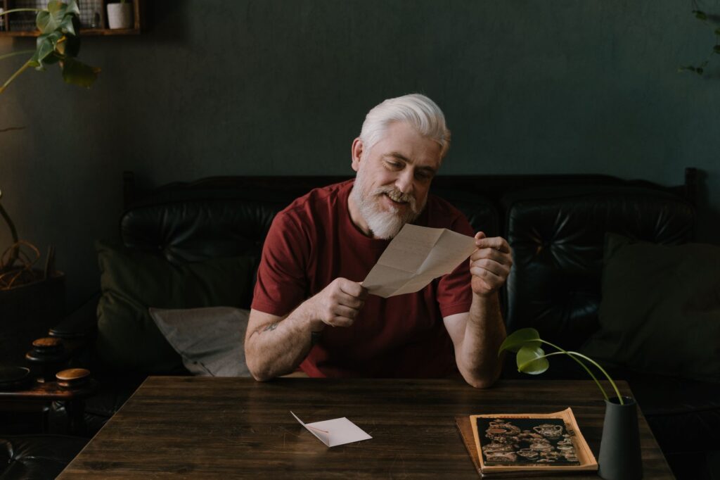 an elderly man with a beard reading a letter at a cozy indoor setting.