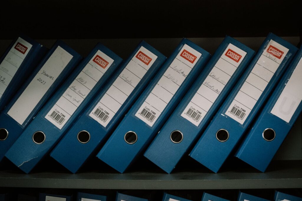 neatly arranged blue office binders labeled with dates and names for organized storage.