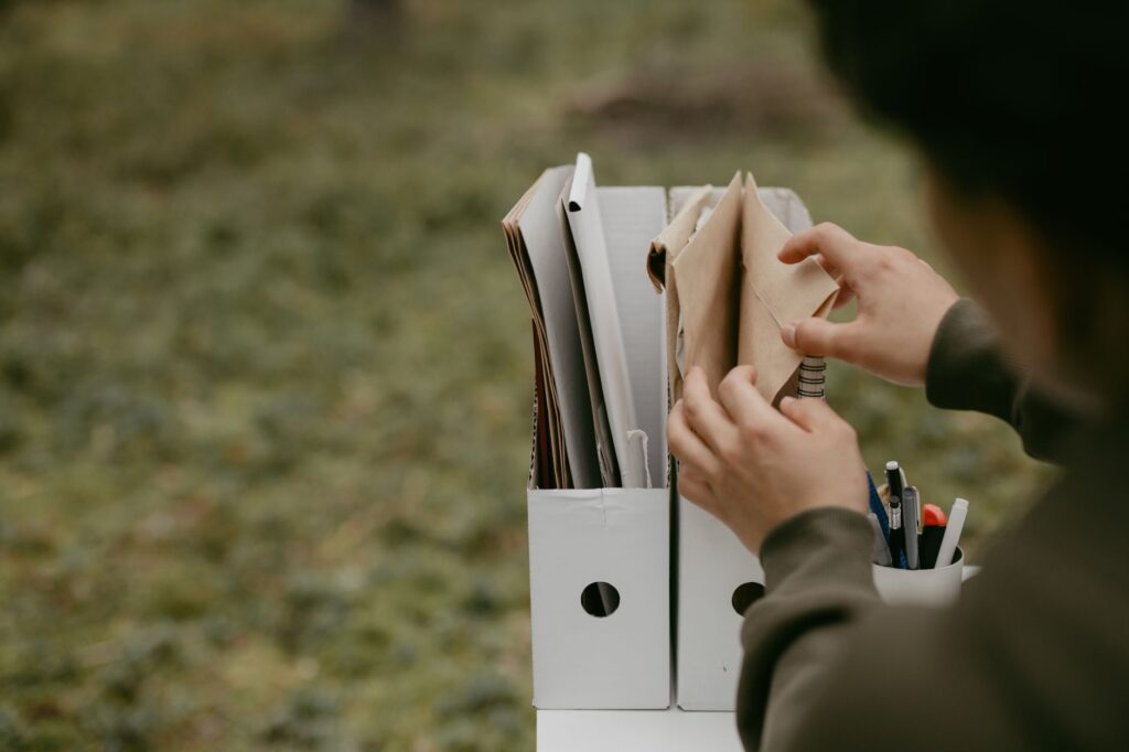 person sorting documents in folders outdoors, hands visible, neutral tone.