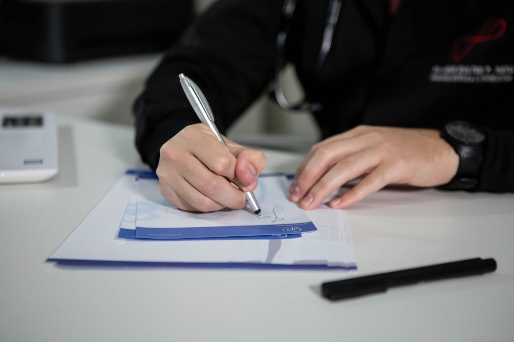 a doctor writing a prescription on paper with a ballpoint pen in a clinic setting.