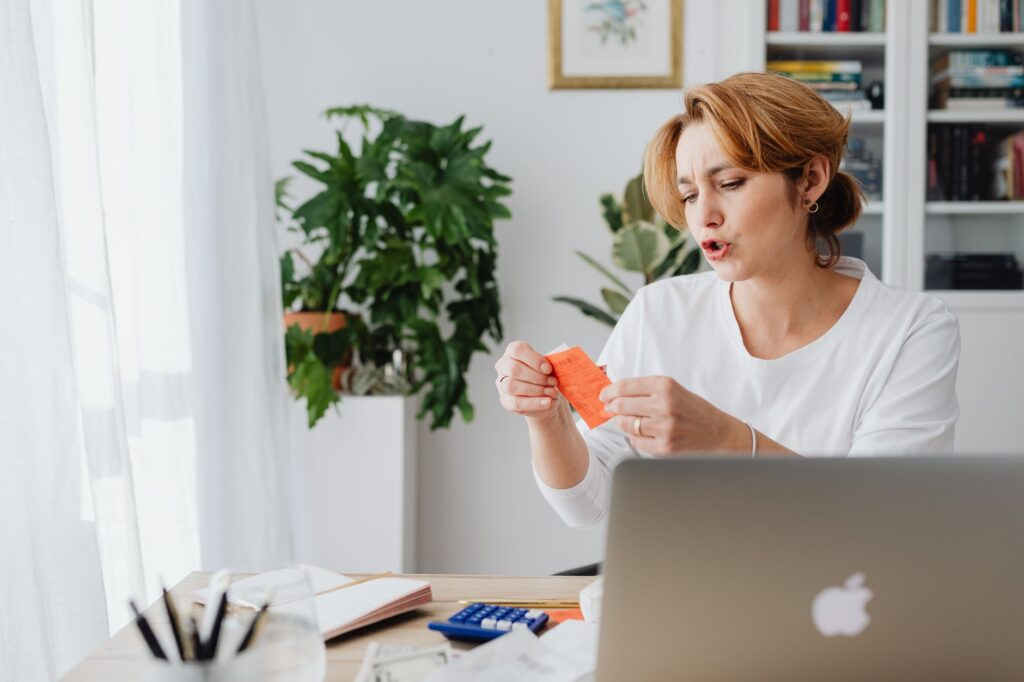 woman reviewing bills at home desk with laptop and plants, managing personal finances.
