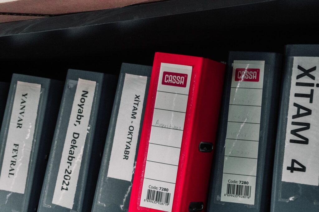color-coded office binders organized neatly in a storage shelf, featuring labels and a striking red binder.
