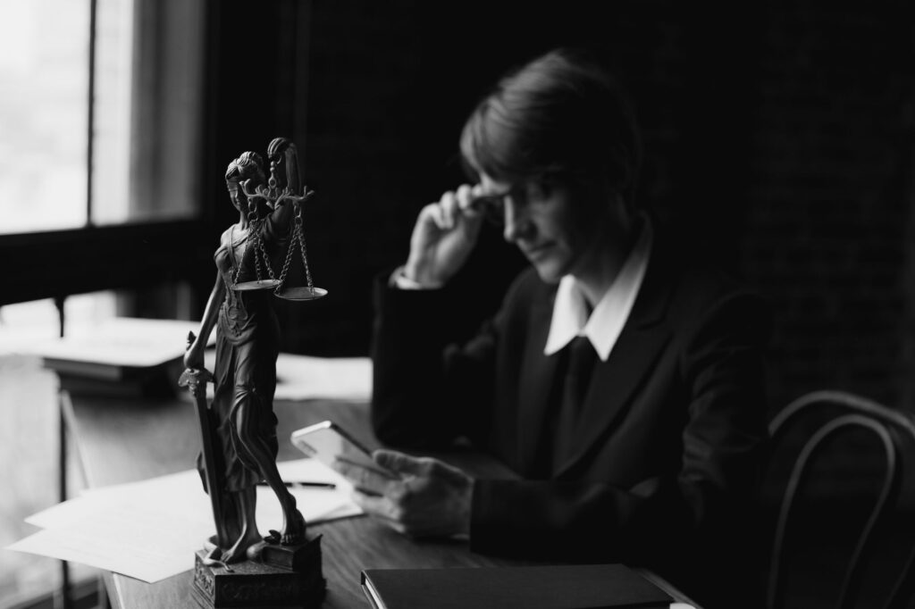 black-and-white image of an attorney in an office with lady justice statue and smartphone, symbolizing modern legal conc